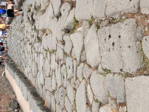 Original stone roadway in Pompeii shows deep cart ruts with tourists walking ahead.