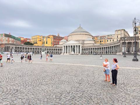 Wide cobbled Piazza del Plebiscito in Naples framed by San Francesco di Paola basilica and colorful palazzi.