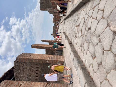 Tourists walk along a restored stone street lined with brick columns in Pompeii.