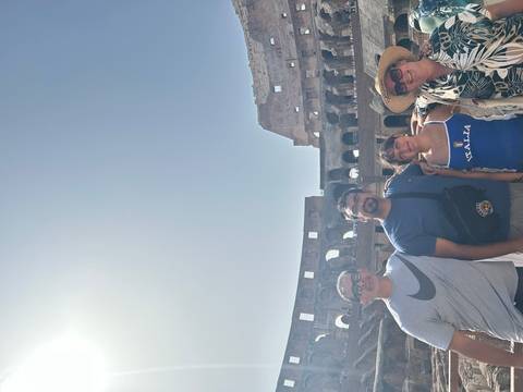 Four travellers smiling inside the sunlit Colosseum with ancient arches in the background.