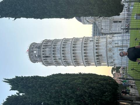 Traveller posing in front of the Leaning Tower of Pisa at dusk with soft golden light in the sky.