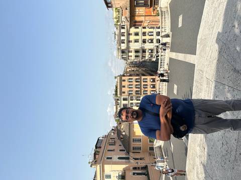 Man standing with arms crossed at the top of the Spanish Steps overlooking Rome’s cityscape.