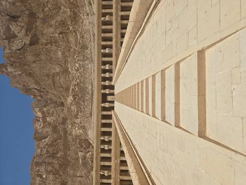 Wide stone ramp leading to the colonnaded Mortuary Temple of Hatshepsut set against rugged cliffs under a clear sky.