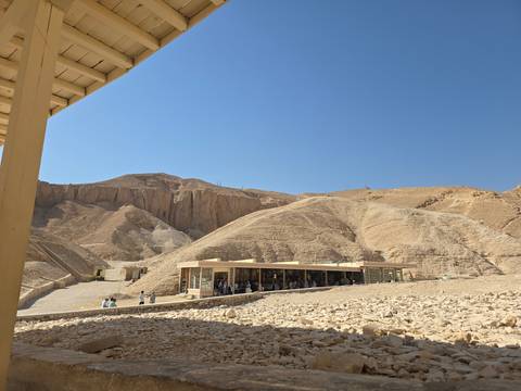 Arid hills and a small visitor centre in the Valley of the Kings under a cloudless blue sky.