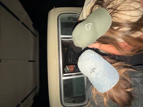 Flash-lit candid inside a safari vehicle at night with two travelers leaning forward to the driver.