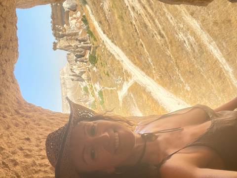 Woman wearing a cowboy hat framed by a cave opening looking out onto Cappadocia fairy chimneys