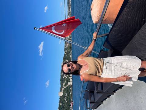 Woman on a yacht deck beside the Turkish flag with Bosphorus and castle ruins behind