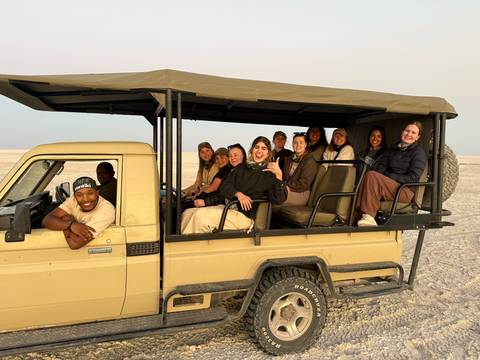 Smiling tour group seated in an open safari Land Cruiser on a vast salt pan