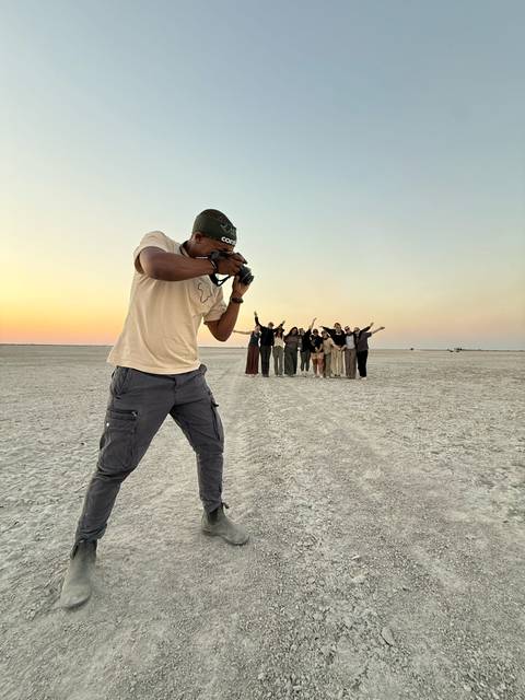 Photographer kneeling on a dry lakebed capturing a jubilant group at sunset