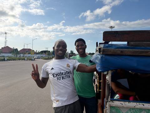 Two young men smiling beside an open truck on a sunny day in an urban lot
