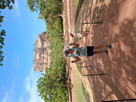 Traveler poses on a path leading to towering Sigiriya Rock fortress rising above the jungle.