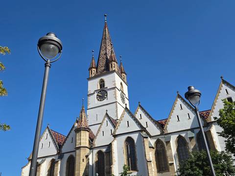 Gothic church with tall patterned spire and clock tower set against a vivid blue sky in an old European town.