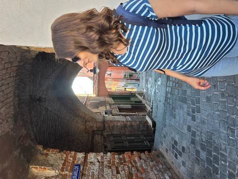 Woman in striped shirt looks down a narrow cobbled alley framed by an old brick archway.