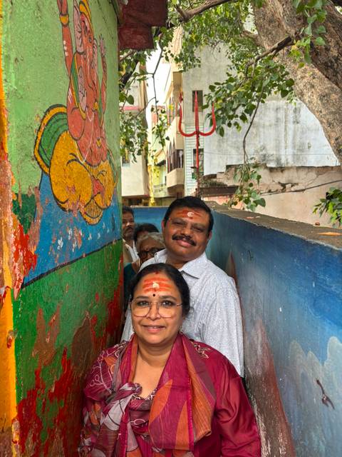 Couple with vermilion marks stand in a narrow alley painted with bright Hindu motifs and trees overhead.