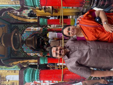 A couple dressed in traditional attire poses in front of a colorful Hindu temple entrance with bells and pillars.