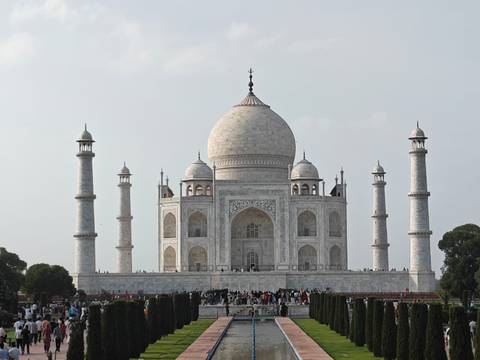 Frontal view of the Taj Mahal with its four minarets and crowds of visitors at the base under a clear sky.