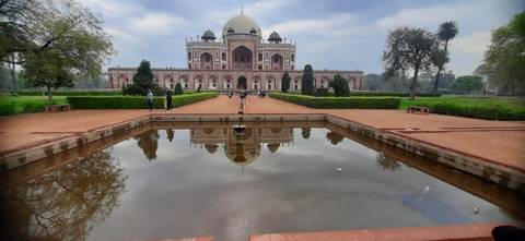 Humayun's Tomb reflected in a rectangular pool with a few visitors walking along the central pathway.