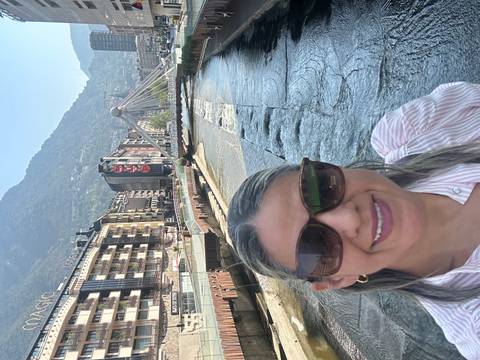 Woman taking a selfie beside a river and modern pedestrian bridge with mountains behind in Andorra La Vella