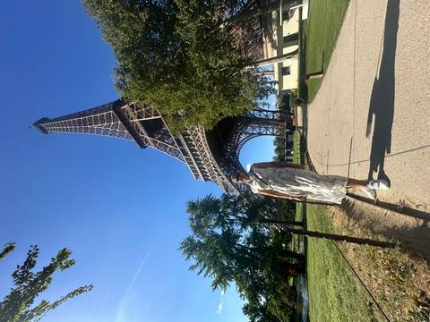 Traveler posing on a path beneath the towering Eiffel Tower on a bright blue-sky day