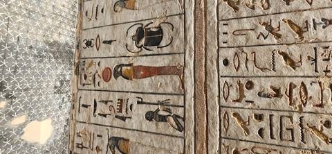 Stone wall panels covered with colorful hieroglyphs and ancient Egyptian figures under a patterned ceiling.