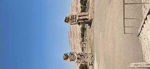 Two colossal seated statues rise from a barren plain with distant hills under a bright blue sky.