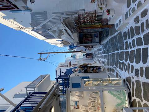 Narrow white-washed alley with blue railings and boutique shops under a clear sky