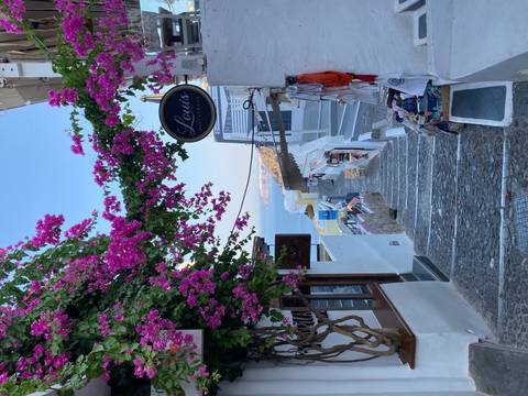 Charming stairway draped with bright pink bougainvillea leading down to the sea between white buildings