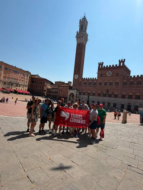 Tour group holding a Travel Chasers banner in Siena’s Piazza del Campo with Torre del Mangia behind