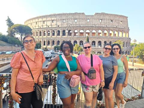 Group of women smiling on a viewpoint railing with the Colosseum in the background