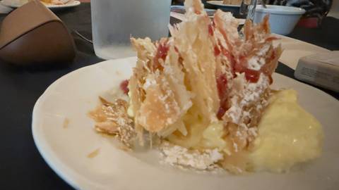 Blurry close-up of a creamy layered pastry topped with puff pastry shards and powdered sugar