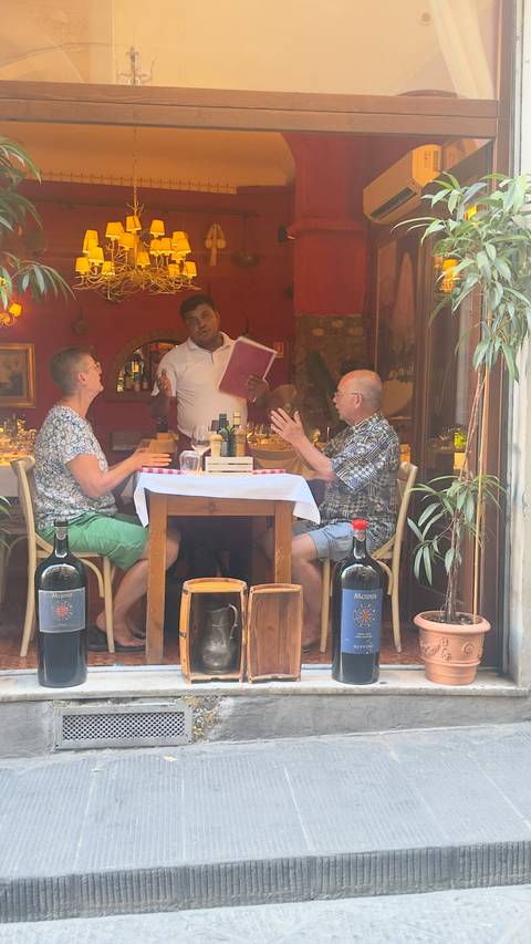 Two diners converse with a waiter over a set table in a cozy restaurant interior.
