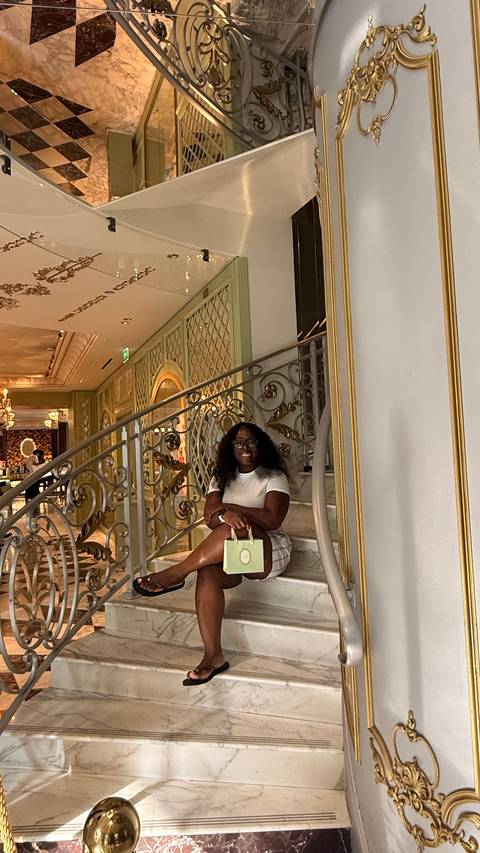 Traveler sits on an ornate marble staircase inside an elegant, luxurious interior holding a shopping bag.