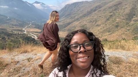 Two friends pose on a mountain overlook with valley, river and peaks stretching into the distance.
