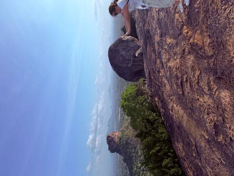 A vast rocky outcrop and surrounding forest plain stretch toward distant mountains under a clear blue sky.