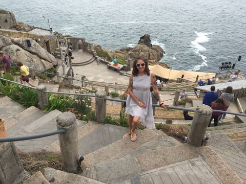 Smiling woman poses on stone steps of Minack Theatre overlooking the rugged coastline