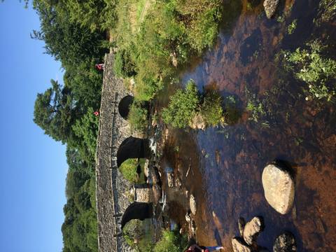Vertical shot of stone bridge spanning a shallow river with two small human figures on top