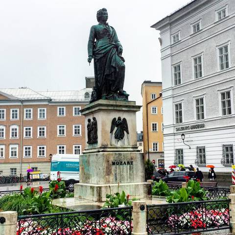 Mozart statue in Salzburg’s Mozartplatz framed by historic pastel buildings on a rainy day