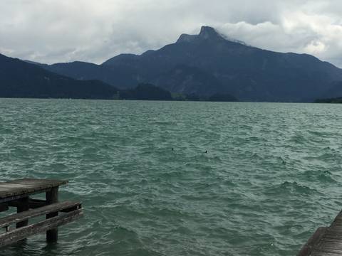 Choppy turquoise lake with wooden jetty and distant mountain backdrop under grey skies