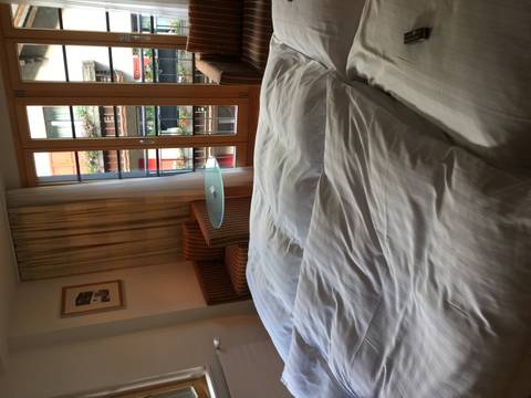Hotel room view across rumpled white bedding toward balcony doors and a small table