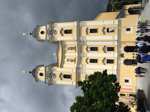 Yellow twin-tower basilica of Mondsee rising against a dramatic dark sky with tourists below