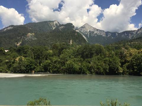 Turquoise river flowing below forested cliffs with high alpine peaks in the background