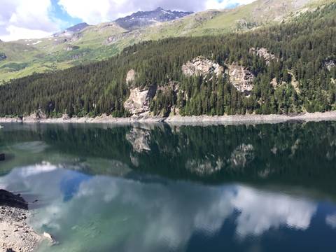 Still alpine reservoir reflecting dense pine forests and rocky slopes under clear skies