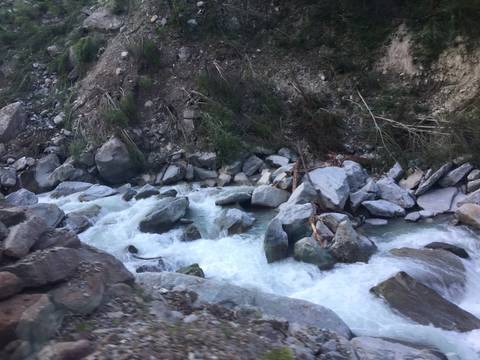Fast-flowing alpine stream crashing over large grey boulders in a rocky gorge