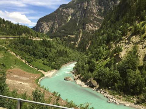Aqua-blue alpine river winding through lush green valley flanked by steep mountains