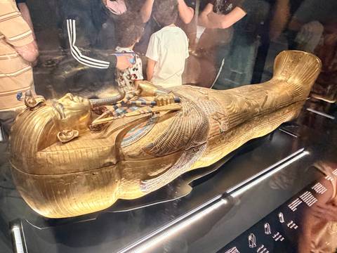 Golden funerary sarcophagus of Tutankhamun displayed in a dimly lit museum surrounded by onlookers.