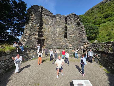 Tour group standing and waving inside the stone ruins of an ancient Scottish castle surrounded by greenery.