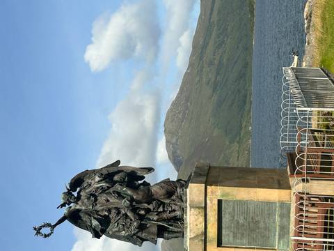 Vertical shot of a lakeside war memorial statue with Scottish Highlands and calm water behind.