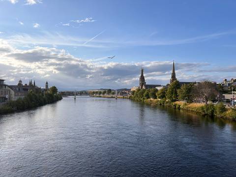 Wide river flowing through Inverness with church spires and historic buildings lining the banks under a dramatic sky.