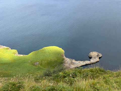 High cliff top covered in lush green grass dropping steeply into the deep blue sea on the Isle of Skye.