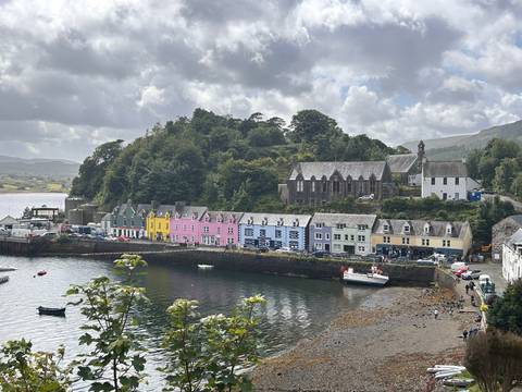 Colorful row of houses lining the harbour at Portree with boats anchored in the water under a cloudy sky.